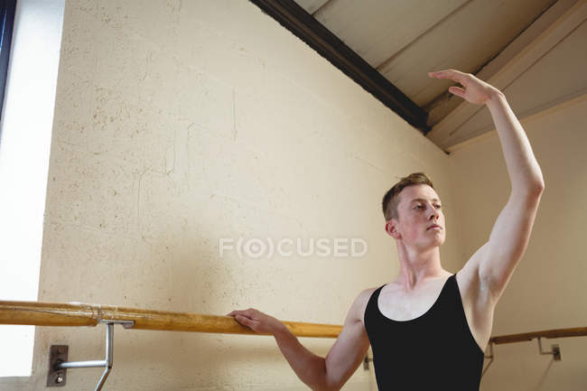 Retrato de bailarino alongamento no barre enquanto pratica dança de balé em estúdio — Fotografia de Stock