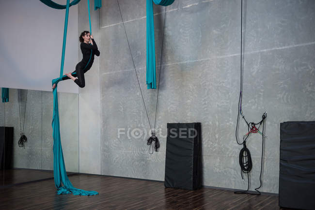 Gymnast exercising on blue fabric rope in fitness studio — Stock Photo