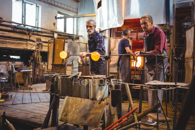 Команда стеклодувов, формирующих стекло на трубах стеклодувного завода — стоковое фото