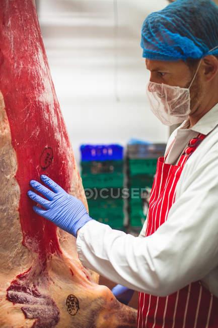 Male butcher touching red meat in storage room — Stock Photo