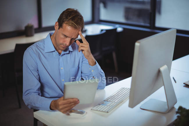 Pensativo hombre de negocios utilizando tableta digital y PC de escritorio en la oficina - foto de stock
