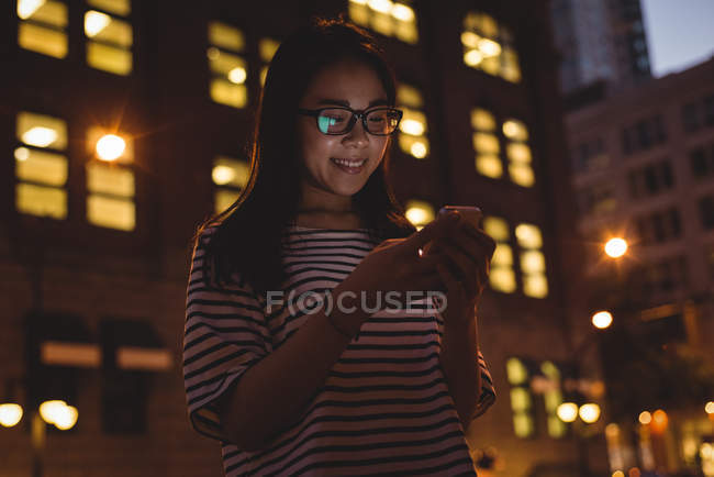 Jeune femme utilisant le téléphone portable dans la ville la nuit — Photo de stock
