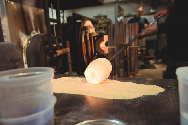 Glassblower rolling molten glass over blowpipe glass on table at glassblowing factory — Stock Photo