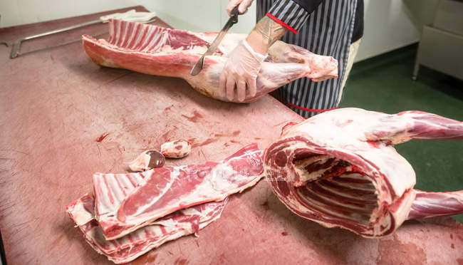 Corte médio de açougueiro cortando as costelas de carcaça de porco no açougue — Fotografia de Stock