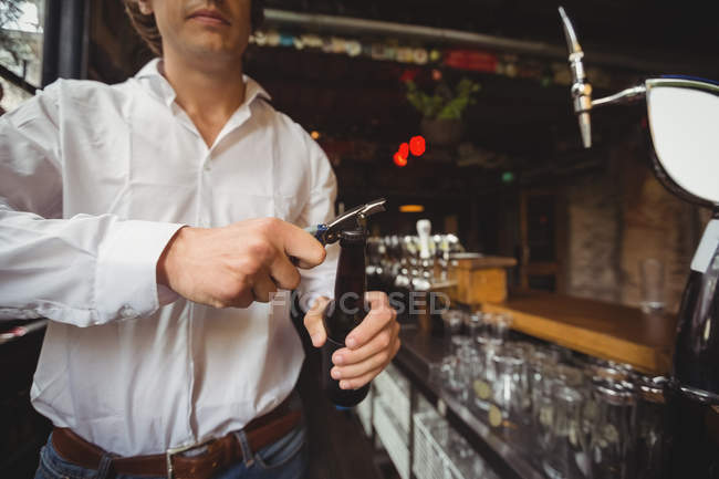 Средняя секция бармена открывает бутылку пива у барной стойки — стоковое фото