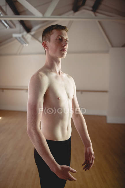 Bailarina sin camisa de pie en un estudio moderno y mirando hacia otro lado - foto de stock