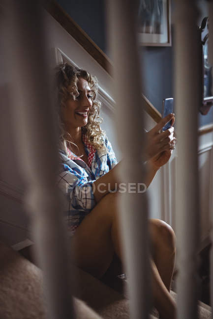 Mulher bonita sentada na escada e usando telefone celular em casa — Fotografia de Stock