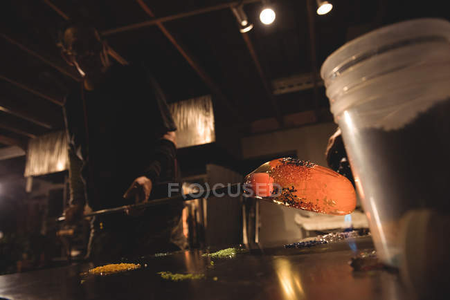 Glassblower rolling molten glass on pieces of colored glass at glassblowing factory — Stock Photo