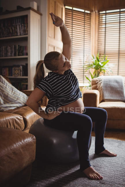 Вагітна жінка виконує розтяжку вправи на фітнес-кулі у вітальні вдома — стокове фото