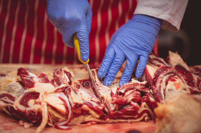 Hands of butcher cutting red meat at butchers shop — Stock Photo
