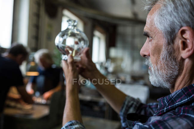 Soplador de vidrio mirando cristalería en fábrica de soplado de vidrio - foto de stock
