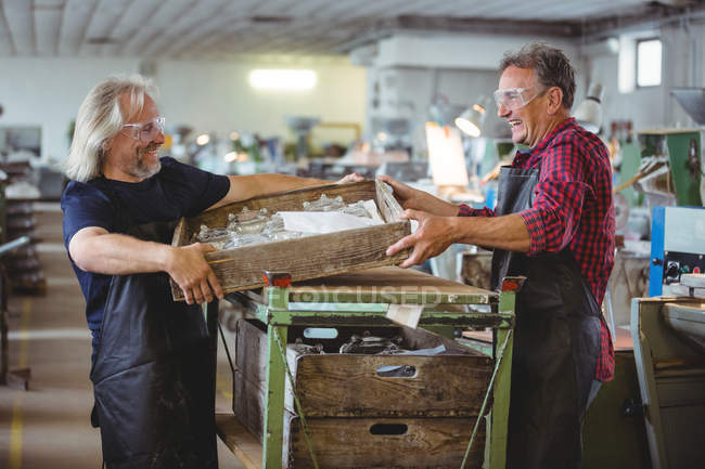 Склоочисник і колега, що тримає дерев'яний контейнер на скляній фабриці — стокове фото
