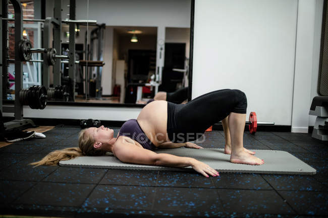 Mujer embarazada realizando ejercicio de estiramiento en el gimnasio - foto de stock
