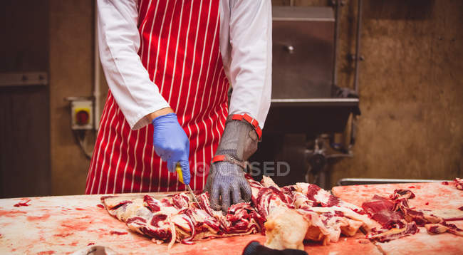 Sección media del carnicero que corta carne roja en la carnicería - foto de stock