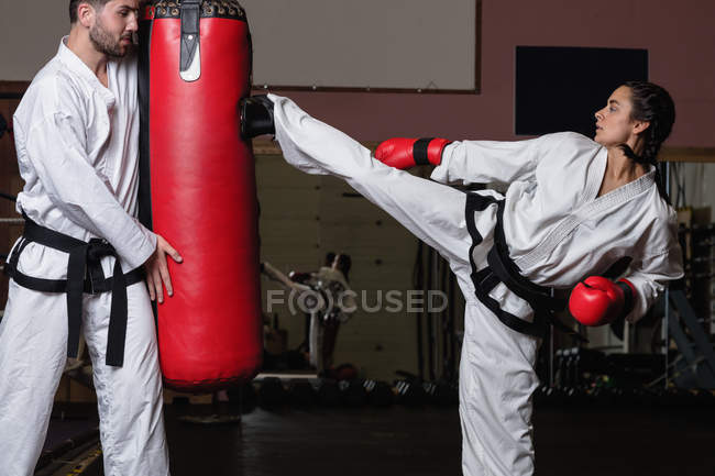 Вид збоку бійців, які практикують карате з мішком для ударів в студії — стокове фото