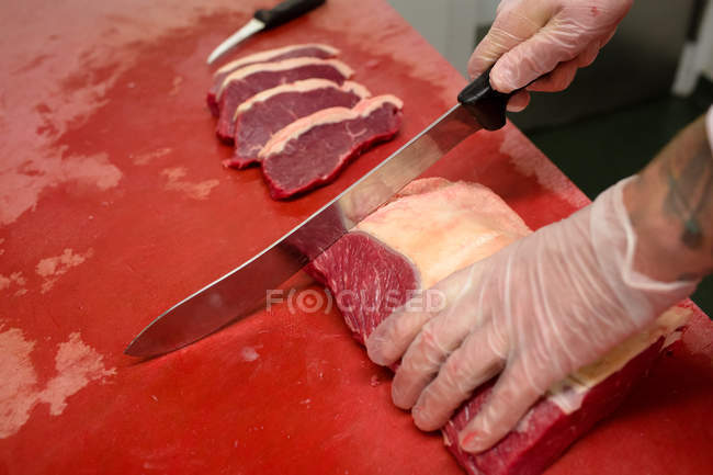 Hands of butcher slicing meat at butchers shop — Stock Photo