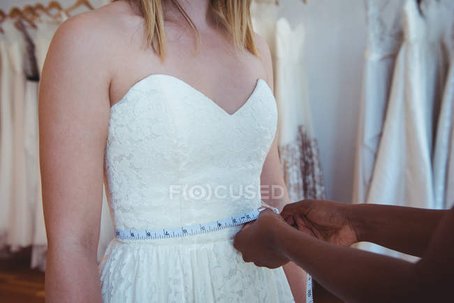 Mujer probándose el vestido de novia con la ayuda del diseñador de moda en el estudio - foto de stock