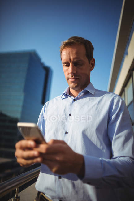 Бізнесмен, використовуючи мобільний телефон, стоячи на балконі в офісі — стокове фото