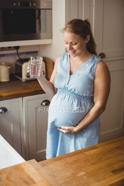 Femme enceinte boire de l'eau dans la cuisine à la maison — Photo de stock