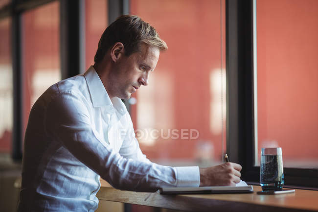 Empresario escribiendo en diario en el escritorio en la oficina - foto de stock