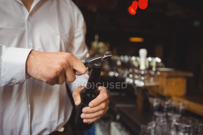 Partie médiane du barman ouvrant une bouteille de bière au comptoir du bar — Photo de stock