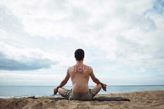 Vue arrière de l'homme effectuant du yoga sur la plage — Photo de stock