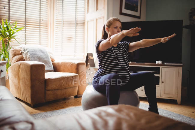 Selective focus of Pregnant woman performing stretching exercise on fitness ball in living room at home — Stock Photo