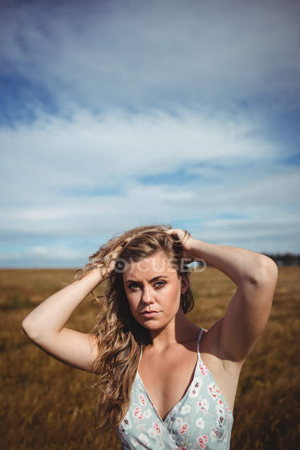 Портрет женщины с руками в волосах, стоящей на пшеничном поле в солнечный день — стоковое фото