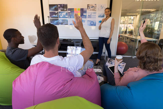 Business executives hand raised while sitting on bean bag during meeting in office — Stock Photo