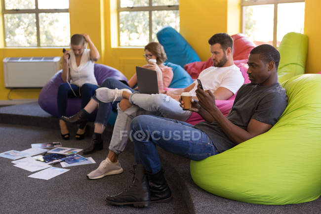 Dirigenti d'azienda che lavorano mentre siedono su beanbag in ufficio — Foto stock