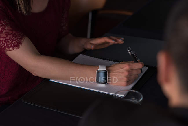 Sección media de la mujer de negocios escribiendo en bloc de notas en la sala de conferencias en el hotel - foto de stock