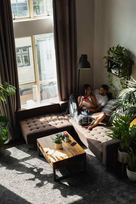 Couple interagissant les uns avec les autres tout en prenant un café dans le salon à la maison — Photo de stock