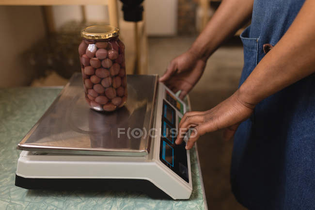 Mid section of male staff weighing jar of nuts on weighing machine — Stock Photo