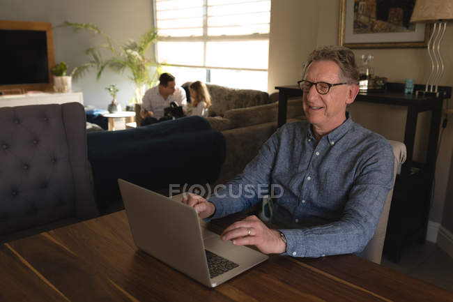 Старший чоловік використовує ноутбук на столі у вітальні вдома — стокове фото