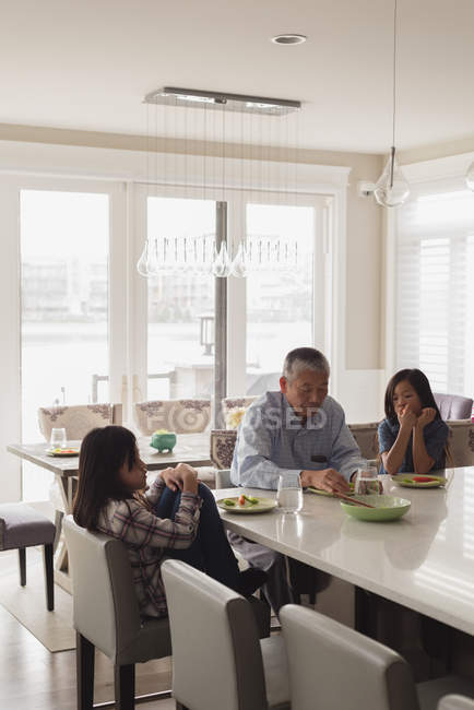 Дедушка и внучки обедают дома. — стоковое фото