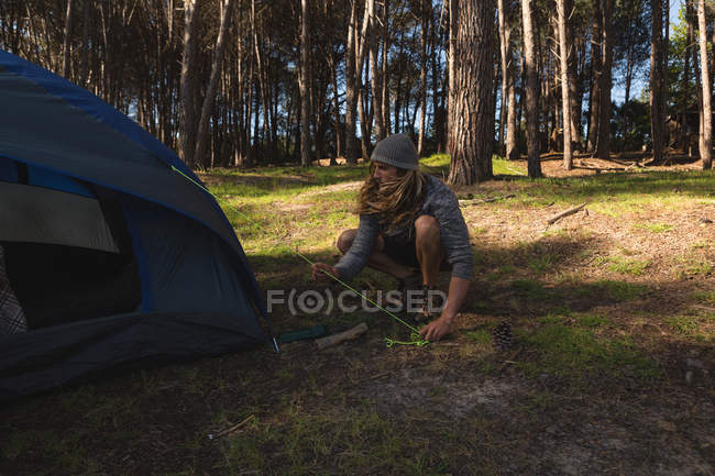 Giovane uomo che mette una tenda nella foresta — Foto stock
