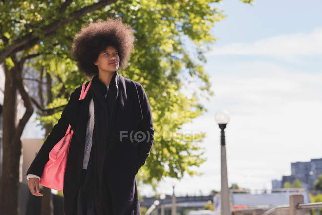 Femme afro réfléchie marchant dans la rue — Photo de stock