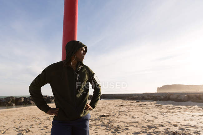 Pensativo atleta masculino manos en la cadera de pie cerca de la playa - foto de stock