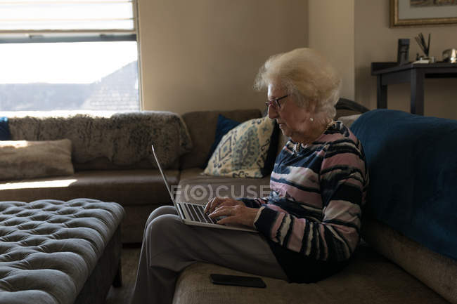 Пожилая женщина использует ноутбук в гостиной дома — стоковое фото