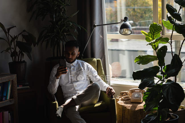 Homem usando telefone celular na cadeira de braço na sala de estar em casa — Fotografia de Stock