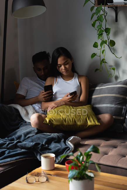 Couple using mobile phone on sofa in living room at home — Stock Photo