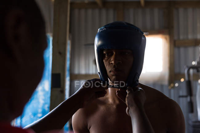 Trainer unterstützt männliche Boxer beim Tragen von Kopfbedeckungen im Boxclub — Stockfoto