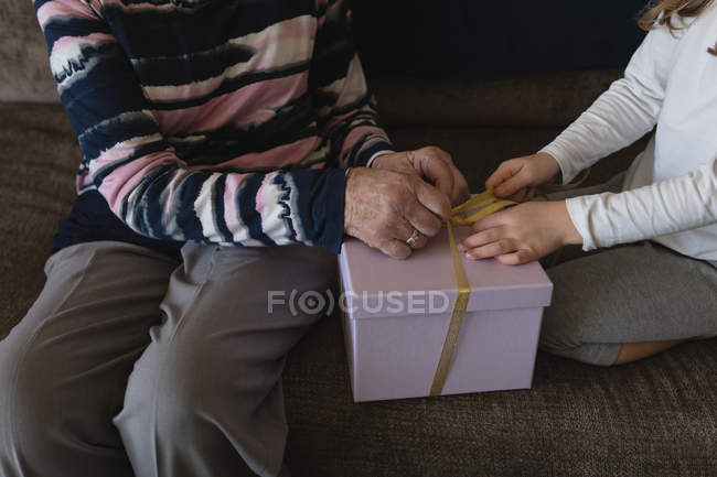 Sección media de la abuela y la nieta abriendo la caja de regalo en casa - foto de stock