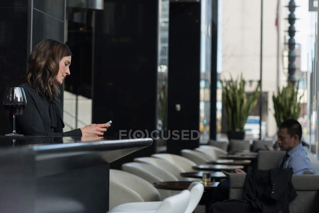 Businesswoman using mobile phone at bar counter while businessman using digital tablet on sofa in hotel — Stock Photo