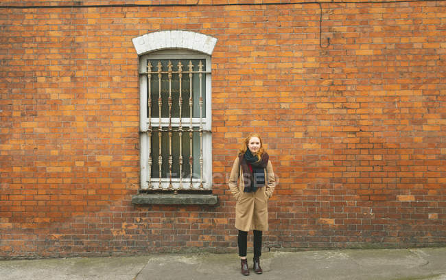 Руда жінка стоїть з рукою в кишені проти цегляної стіни — стокове фото