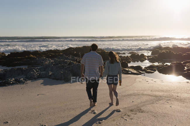 Rückansicht des Paares, das sich an Händen hält und am Strand spaziert — Stockfoto