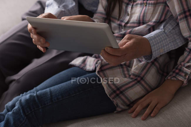 Mid section of grandfather and granddaughter using digital tablet on sofa in living room at home — Stock Photo