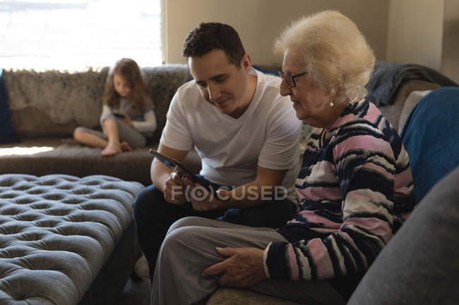 Madre e hijo usando tableta digital en el sofá en la sala de estar en casa - foto de stock