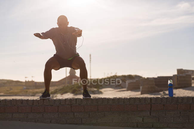 Male athlete exercising on surrounding wall near beach — Stock Photo