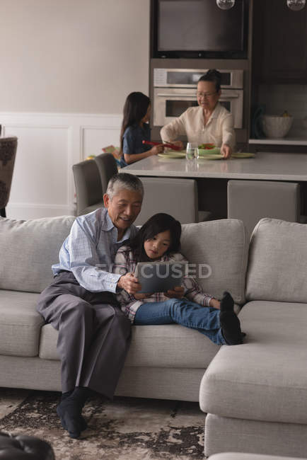 Grandfather and granddaughter using digital tablet on sofa in living room at home — Stock Photo
